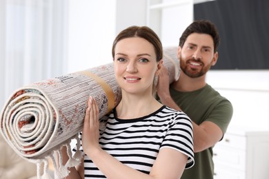 Photo of Smiling couple holding rolled carpet in room