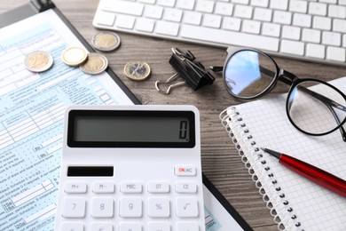 Photo of Tax accounting. Calculator, document, stationery and coins on wooden table, closeup