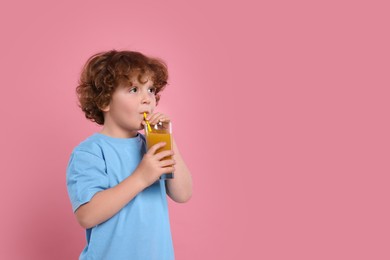 Cute little boy drinking fresh juice through straw on pink background, space for text
