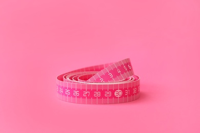Photo of New measuring tape on pink background, closeup