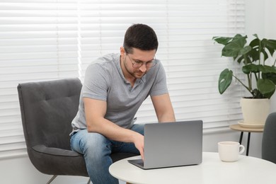 Photo of Man working with laptop at table in living room
