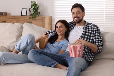 Photo of Happy couple watching show at home. Woman changing TV channels with remote control