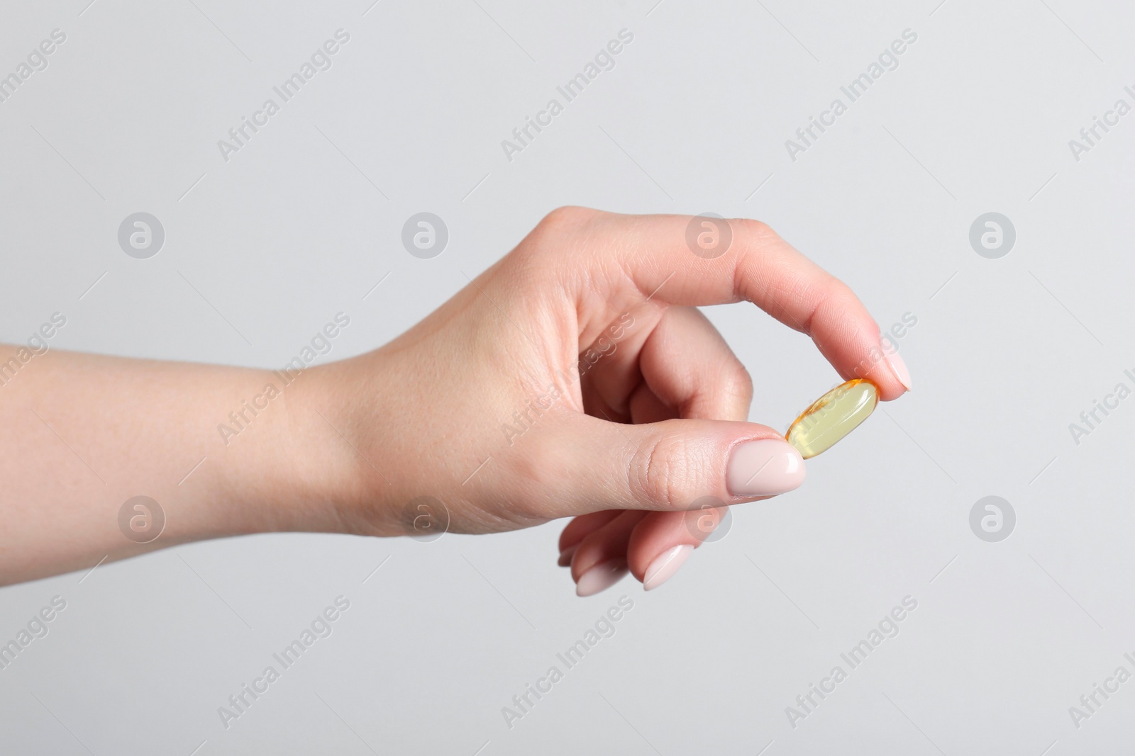 Photo of Woman holding vitamin capsule on light grey background, closeup. Health supplement