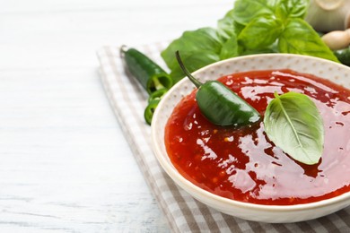 Photo of Spicy chili sauce with basil on white wooden table, closeup. Space for text