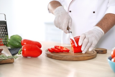 Photo of Professional chef cutting pepper on table in kitchen, closeup
