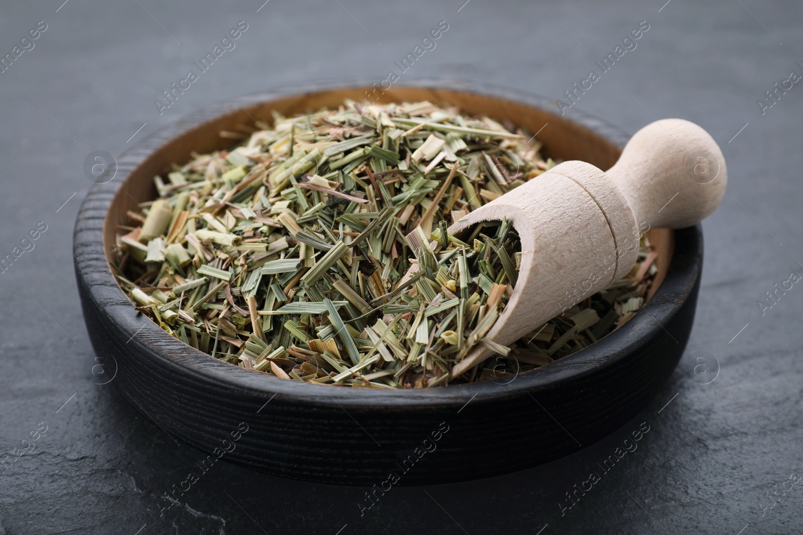 Photo of Bowl with aromatic dried lemongrass and scoop on black table, closeup