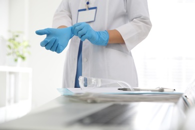 Photo of Doctor putting on medical gloves near table in office, closeup