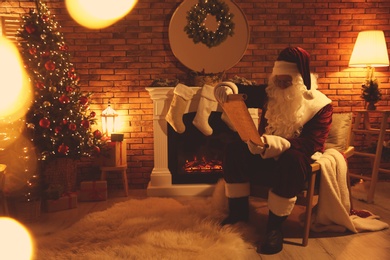 Photo of Santa Claus reading wish list near fireplace indoors