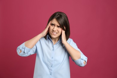 Photo of Young woman suffering from migraine on crimson background