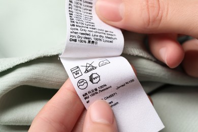 Photo of Woman holding clothing labels on light green garment, closeup