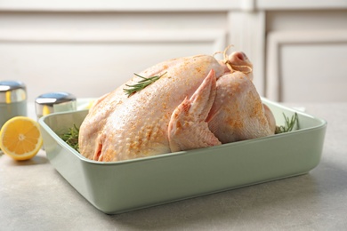 Photo of Baking dish with raw spiced turkey and rosemary on table