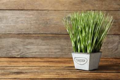 Photo of Artificial plant in metal flower pot on wooden table. Space for text