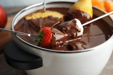 Photo of Dipping fresh fruits into pot with tasty chocolate fondue, closeup