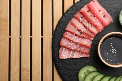 Photo of Tasty sashimi (pieces of fresh raw tuna), cucumber slices and soy sauce on wooden table, top view. Space for text