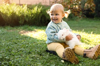 Photo of Happy little girl with cute rabbit on green grass outdoors. Space for text