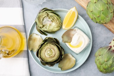 Photo of Delicious cooked artichokes with tasty sauce served on grey table, flat lay