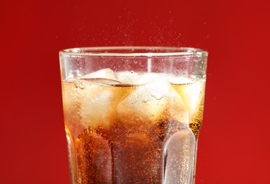 Photo of Glass of refreshing soda drink with ice cubes on red background, closeup