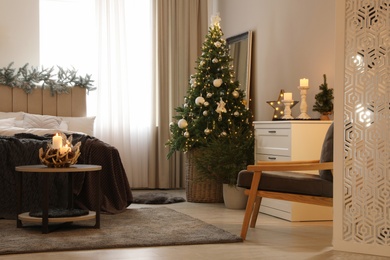 Photo of Beautiful decorated Christmas tree with fairy lights in bedroom interior