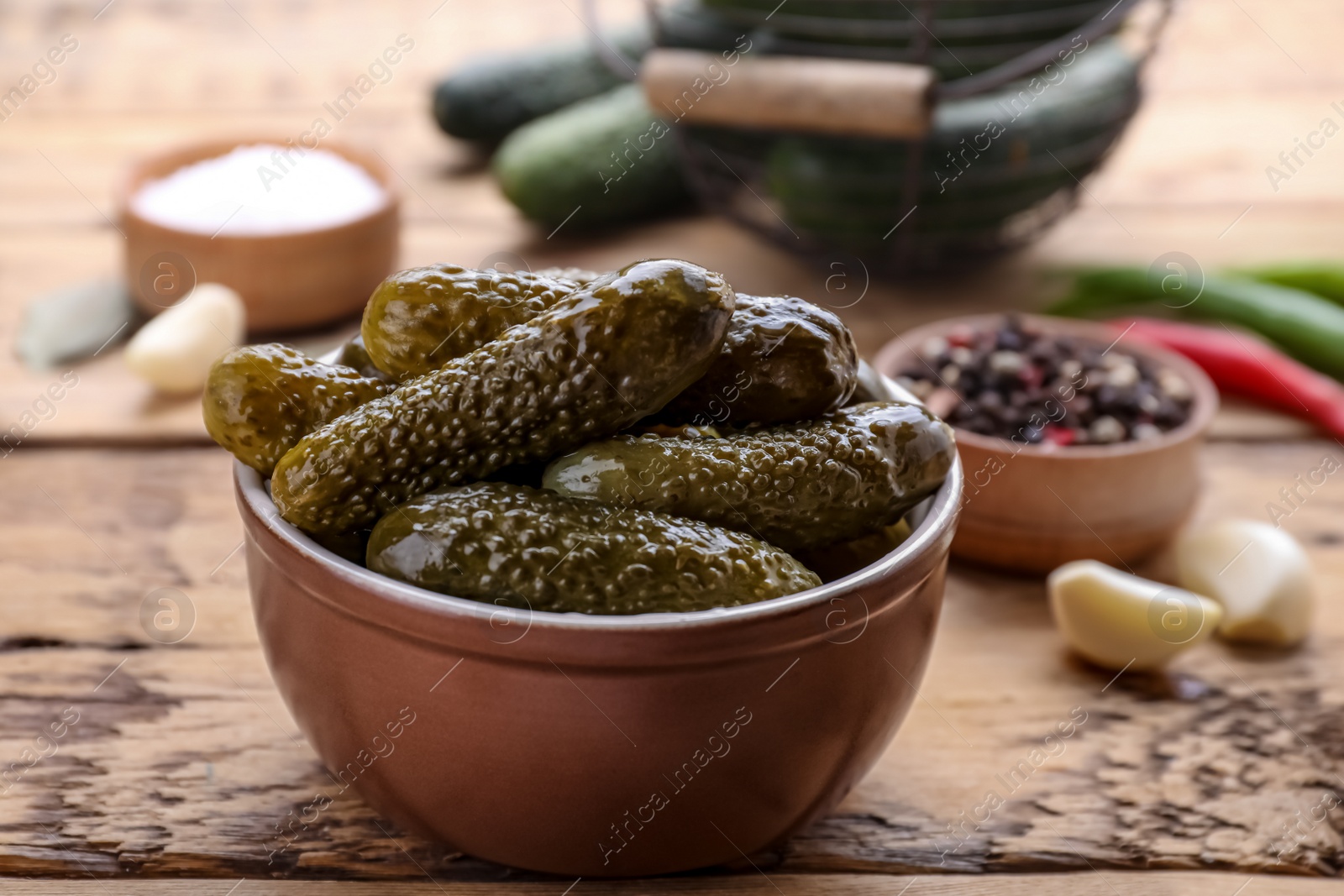 Photo of Bowl of pickled cucumbers and ingredients for food preservation on wooden table