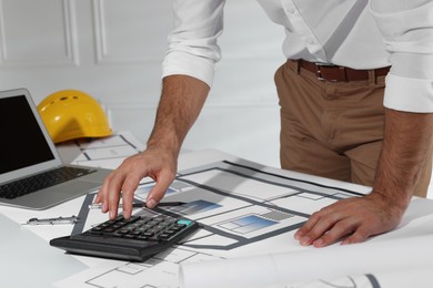 Photo of Architect working with construction drawings and calculator indoors, closeup