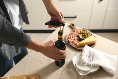 Photo of Man opening wine bottle with corkscrew at table indoors, closeup