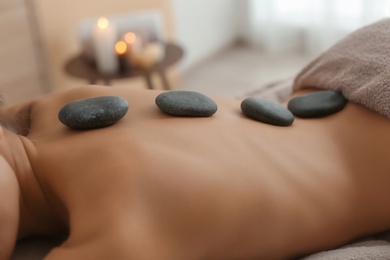 Photo of Beautiful young woman getting hot stone massage in spa salon