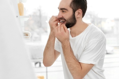 Photo of Young man flossing his teeth indoors