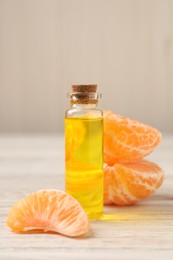Photo of Bottle of tangerine essential oil and fresh fruit on white wooden table