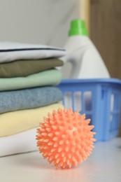 Photo of Orange dryer ball on white table near stacked clean clothes, closeup