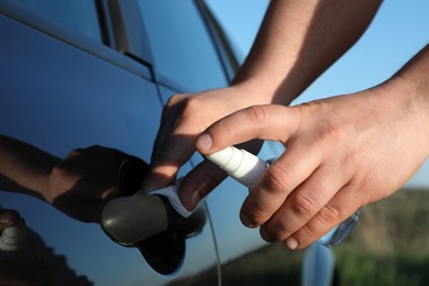 Photo of Closeup view of man disinfecting car door handle outdoors