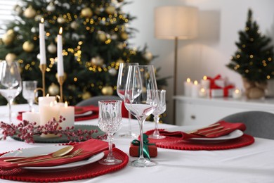 Photo of Christmas table setting with burning candles, gift box and dishware indoors