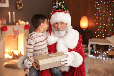 Photo of Little child with Santa Claus and Christmas gift at home