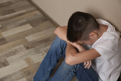Photo of Upset boy sitting on floor at wall. Space for text