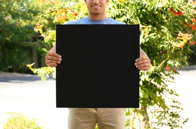 Photo of Man holding black empty poster outdoors, closeup. Space for design