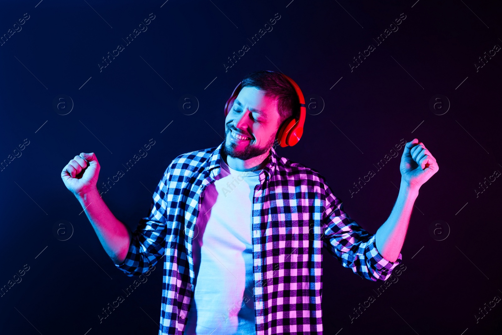 Photo of Happy man in headphones enjoying music in neon lights against dark blue background