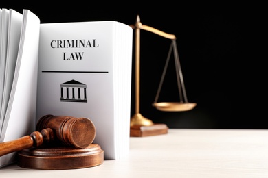 Photo of Judge's gavel, Criminal Law book and scales on white table against black background. Space for text