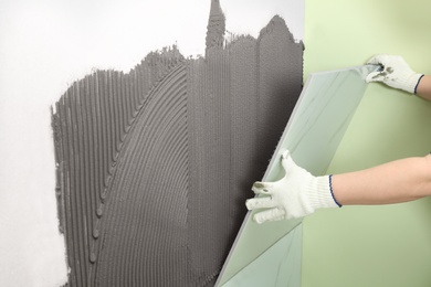Photo of Worker installing ceramic tile on wall, closeup. Space for text