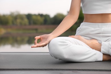 Photo of Woman practicing Padmasana on yoga mat outdoors, closeup and space for text. Lotus pose
