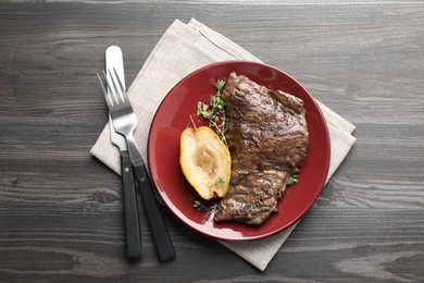 Photo of Delicious roasted beef meat served with caramelized pear and thyme on grey wooden table, flat lay
