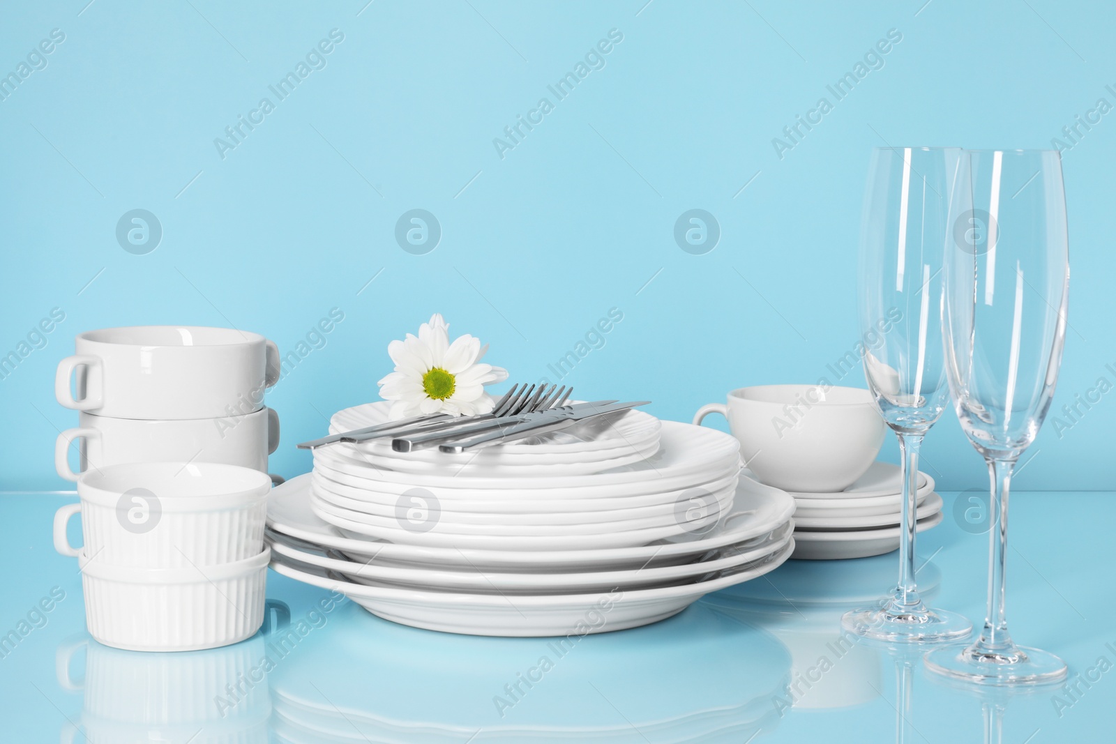 Set of clean dishes, glasses and cutlery on light blue table Photo of Set of clean dishes, glasses and cutlery on light blue table