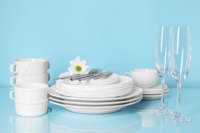 Photo of Set of clean dishes, glasses and cutlery on light blue table
