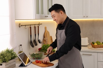 Photo of Cooking process. Man using tablet while cutting tomatoes in kitchen