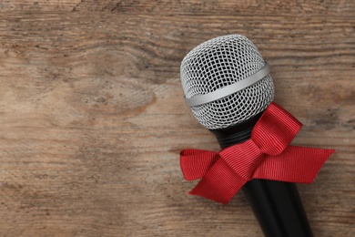 Photo of Top view of microphone with red bow on wooden table, space for text. Christmas music