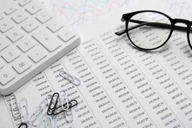 Photo of Glasses, paper clips and calculator on accounting documents with data, closeup