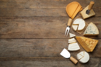 Photo of Set of different cheeses and specialized knives and fork on wooden table, flat lay. Space for text