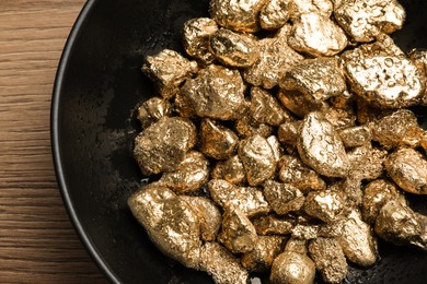 Photo of Bowl of gold nuggets on wooden table, top view