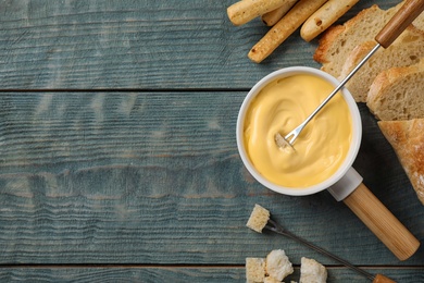Flat lay composition with pot of tasty cheese fondue on blue wooden table, space for text