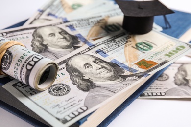 Photo of Dollar banknotes, mini student graduation hat and book on white background. Tuition fees concept