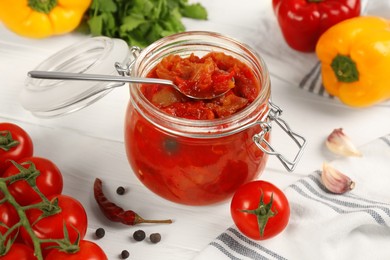 Photo of Glass jar of delicious canned lecho and fresh ingredients on white wooden table, closeup