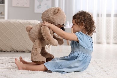 Photo of Cute little girl with teddy bear on floor at home